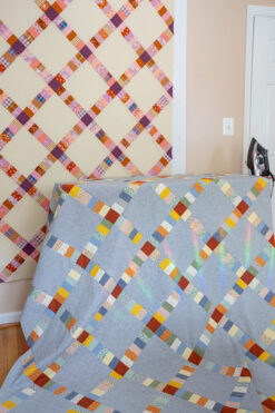 Two Simply Scraps quilt tops, one hanging on the wall and one on an ironing board.