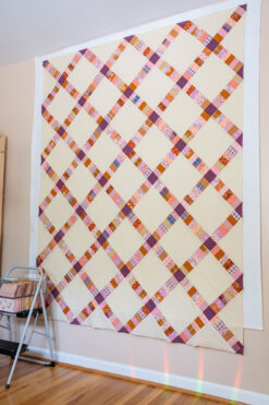 Simply Scraps quilt top in a variety of pink, purple and caramel fabrics hanging on a wall.