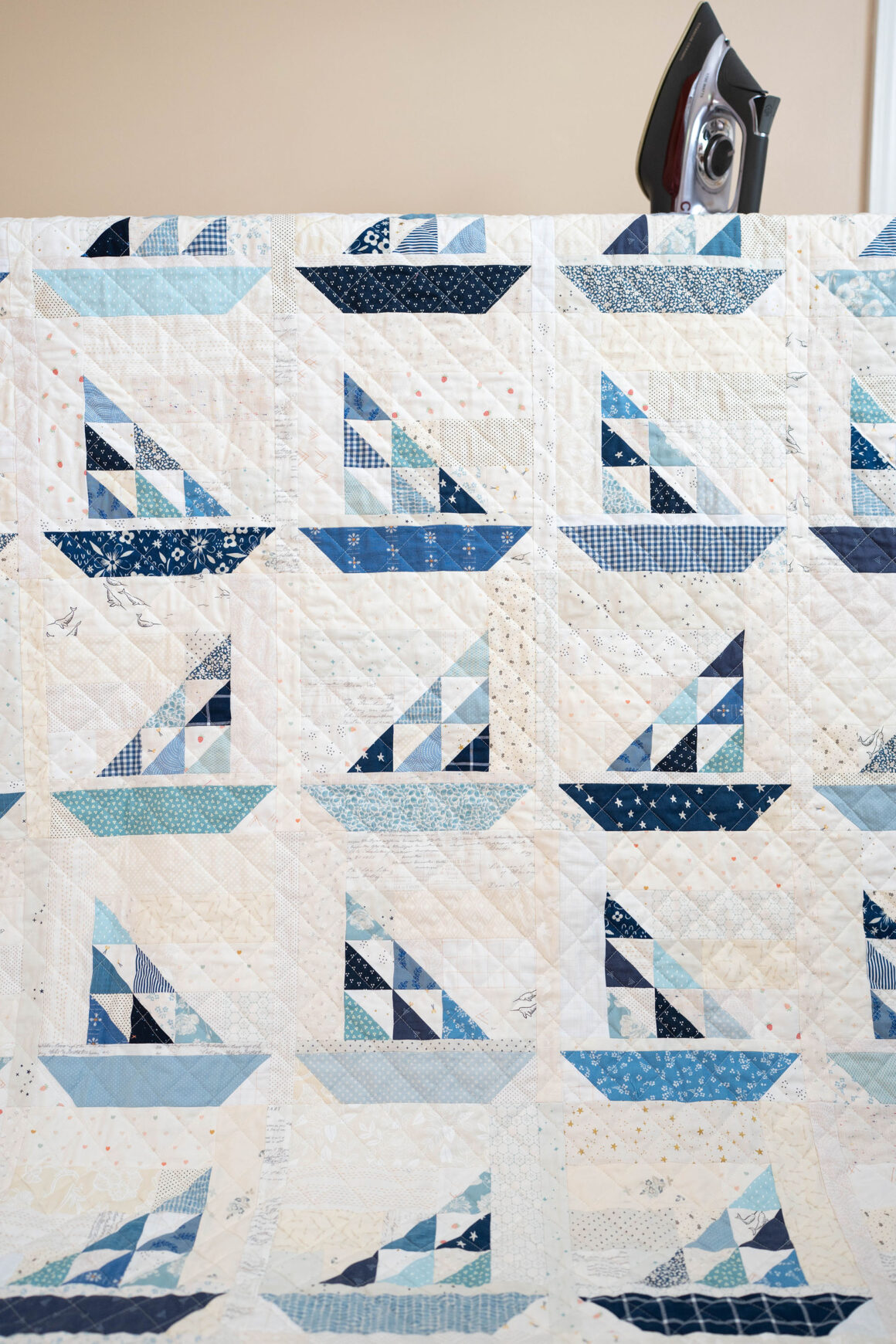 A patchwork quilt in a variation of blues and neutrals forming little sailboats.