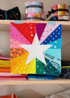 A white star sitting in front of a rainbow burst of color. This is a foundation paper pieced quilt block template.